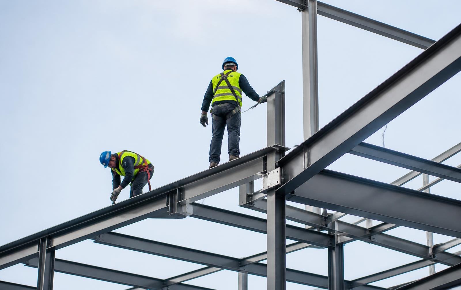 Steel erectors working at height in harnesses on a UK construction frame